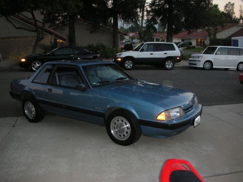 1990 Ford Mustang - Blue 1990 Ford Mustang is parked in front of a house with other vehicles behind it.