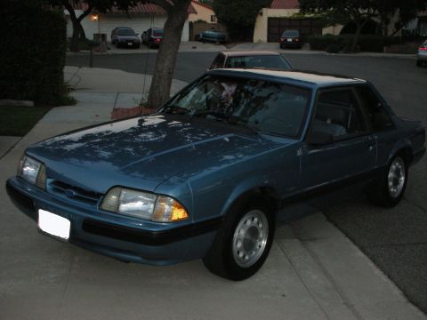1990 Ford Mustang - A blue 1990 Ford Mustang is parked in front of a house on a suburban street.