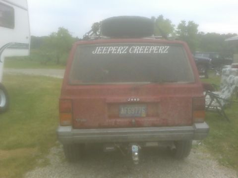 1992 Jeep Cherokee - Rear view of a red Jeep Cherokee with a spare tire mounted on the roof rack and a custom sticker on the back window.