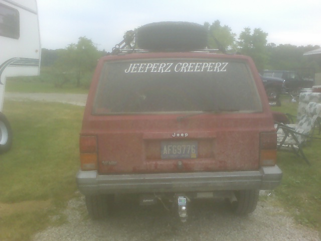 red Jeep Cherokee with spare tire on roof rack and 'JEEPERZ CREEPERZ' sticker on rear window