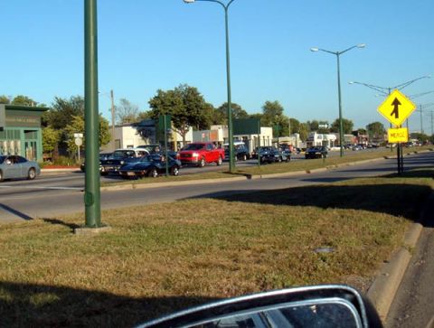 1971 Ford Ranchero - A line of cars, including a 1971 Ford Ranchero, are visible on a street with a merge sign in the background.