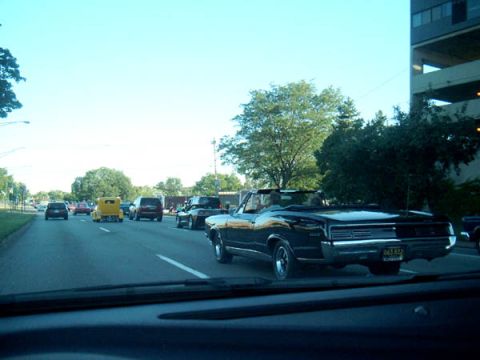 1971 Ford Ranchero - A black convertible cruises down the road with other vehicles in traffic.
