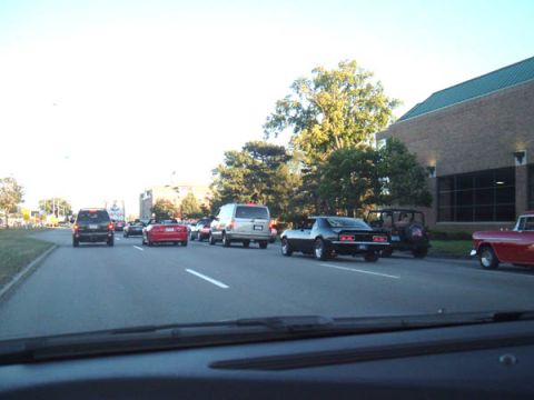 1971 Ford Ranchero - Multiple vehicles are seen on the road during a car event, with a building in the background.