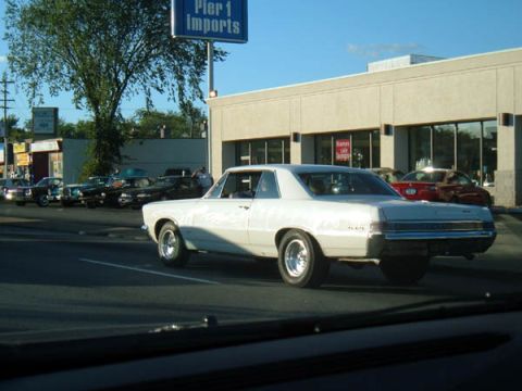 1971 Ford Ranchero - A white coupe with chrome wheels drives past a commercial building.