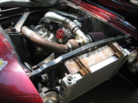 1969 Ford Mustang - The engine bay of a car features a turbocharger and custom piping, with a large radiator in front.