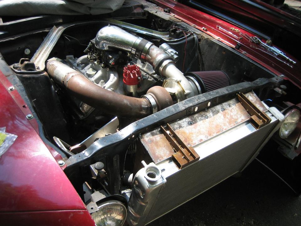 Engine bay with a turbocharger, intercooler piping, and a large radiator. Red car exterior visible