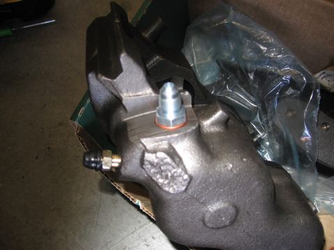 1994 Ford Bronco - A dark gray brake caliper with a silver bleeder valve and copper washer is shown in detail.