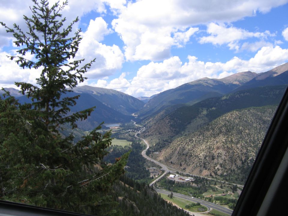 Mountain valley landscape with a winding road, a lake, and trees under a cloudy sky