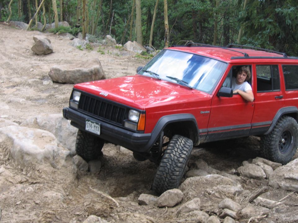 Red 1996 Jeep Cherokee on rocky terrain, driver visible