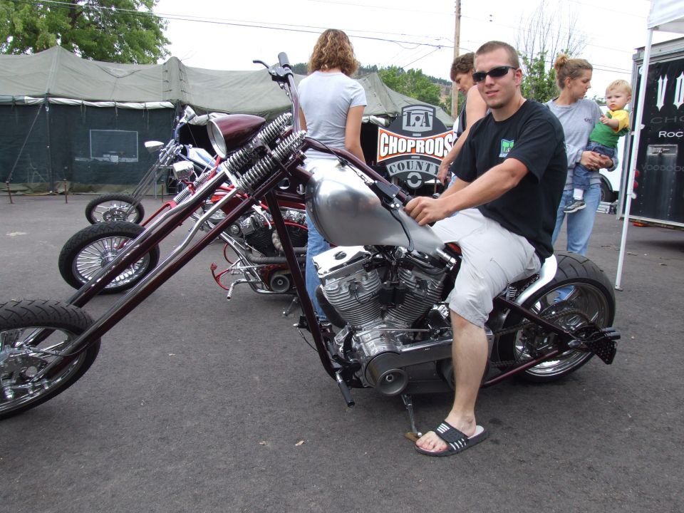 Custom motorcycle with a man sitting on it, showing a large engine and spoked wheels