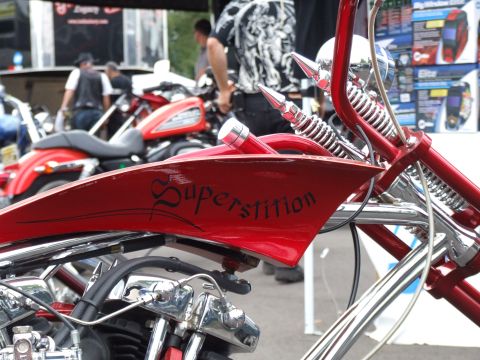 1997 Jeep TJ - A custom motorcycle with 'Superstition' painted on its red fuel tank is shown, with other bikes and people in the background.