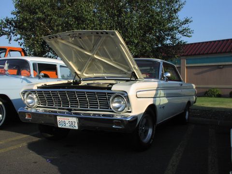 1979 Ford Bronco - A cream 1963 Ford Falcon is displayed with its hood open, parked alongside other vehicles in a lot.