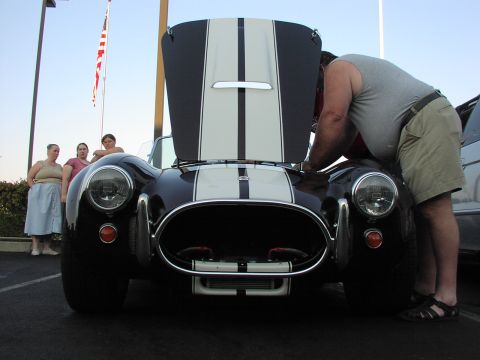 1979 Ford Bronco - A dark blue and white striped sports car is viewed from the front with its hood open, as a man inspects the engine.