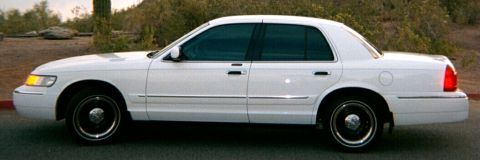 2001 Mercury Grand Marquis - Side profile of a white 2001 Mercury Grand Marquis sedan parked on a road with desert foliage in the background.