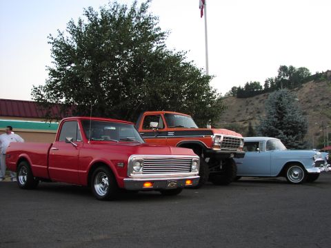 1979 Ford Bronco - Three classic trucks and cars are parked in a lot, with the orange Ford F-Series truck prominently displayed.