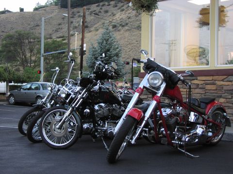1979 Ford Bronco - Several custom motorcycles are parked in a row outside a building with stone and glass facade.