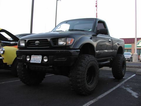 1979 Ford Bronco - Modified black Toyota Tacoma pickup truck with flame decals and oversized tires parked in a lot.