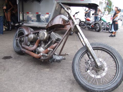 1997 Jeep TJ - A custom motorcycle with a brown fuel tank and rusty exhaust pipes is parked outdoors near a trailer and other motorcycles.