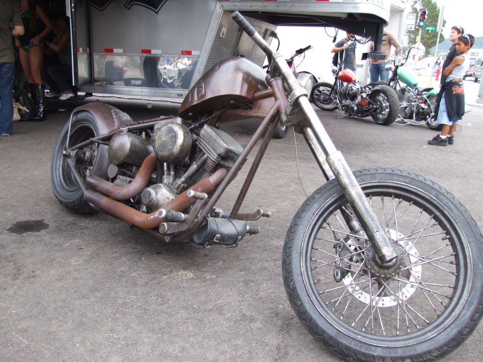 Brown custom motorcycle with exposed engine and rusty exhaust pipes, parked in front of a trailer