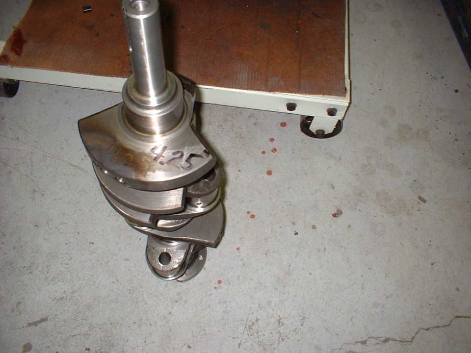 Crankshaft with "4.25" written on it, resting on a concrete floor near a cart