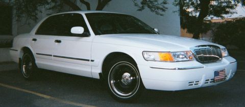 2001 Mercury Grand Marquis - A white 2001 Mercury Grand Marquis is parked in a lot with a tree in the background.