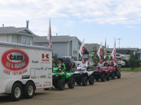 1995 Ford Bronco - A line of ATVs, some with riders, are parading down a residential street, accompanied by a trailer.