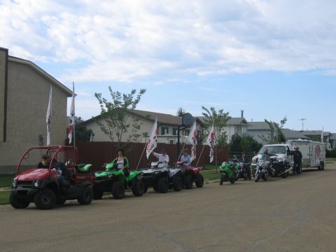 1995 Ford Bronco - A procession of ATVs and motorcycles moves down a suburban street, some carrying flags.