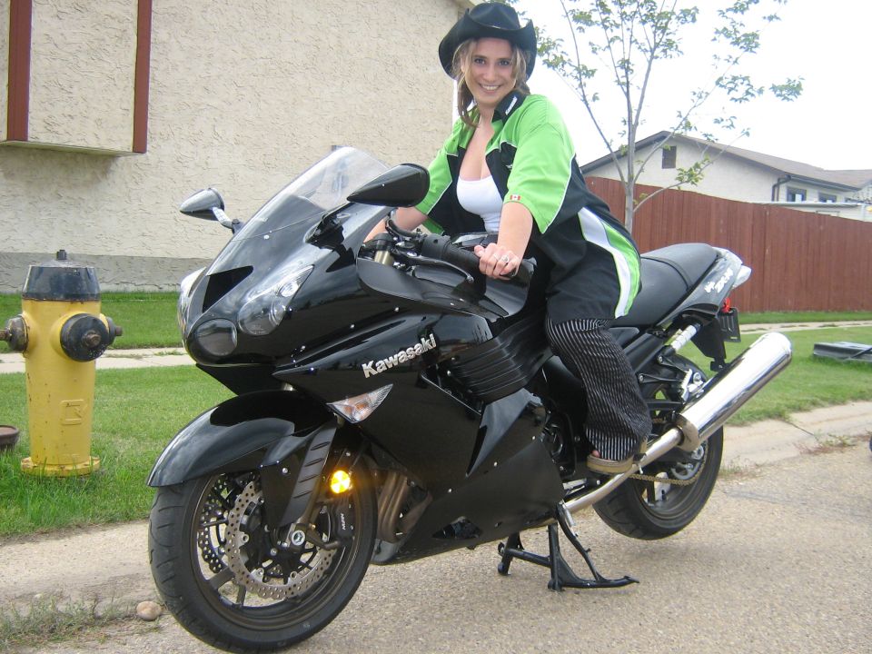 Black Kawasaki sport bike with rider in green jacket, front 3/4 view on a driveway