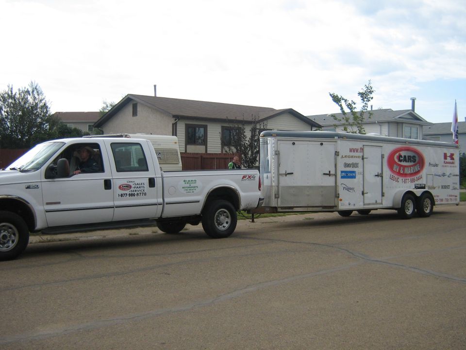 White pickup truck towing a white trailer with various logos and text