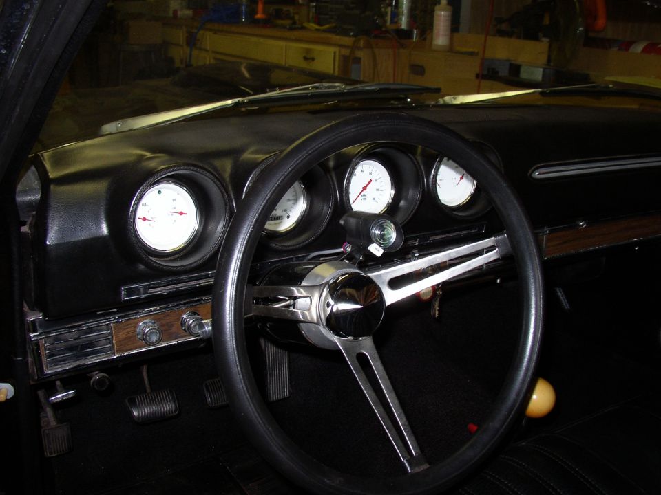 Dashboard of a 1969 Ford Ranchero with three gauges, a black steering wheel, and wood-grain trim
