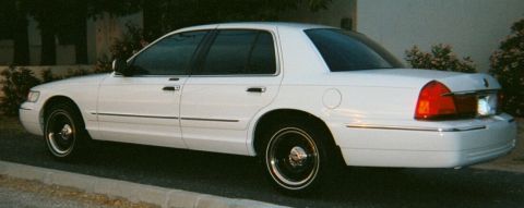 2001 Mercury Grand Marquis - A white 2001 Mercury Grand Marquis is parked curbside with trees in the background.