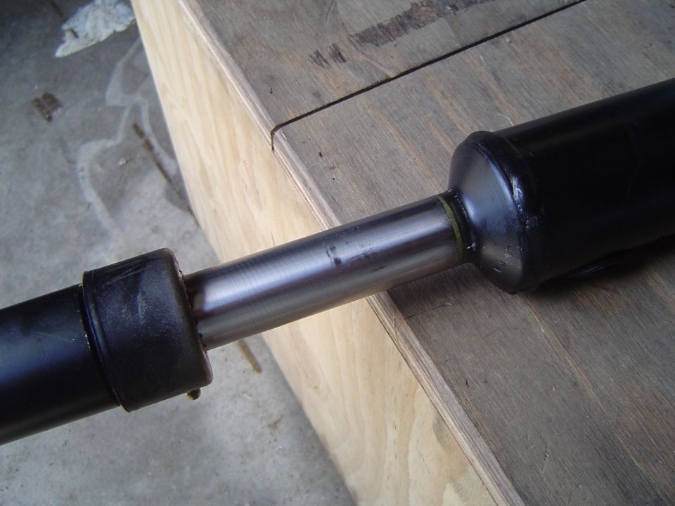 Extended black shock absorber on a plywood bench showing polished shaft and bump stop