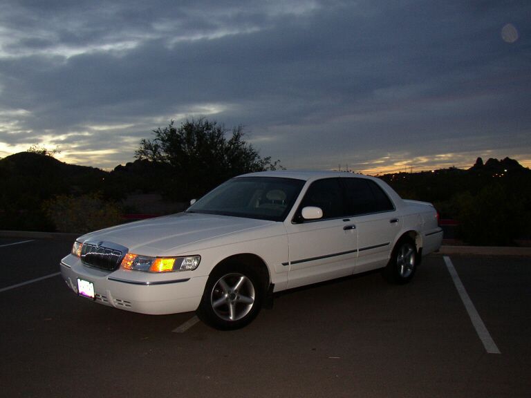 White Mercury Grand Marquis sedan parked at dusk with desert hills behind