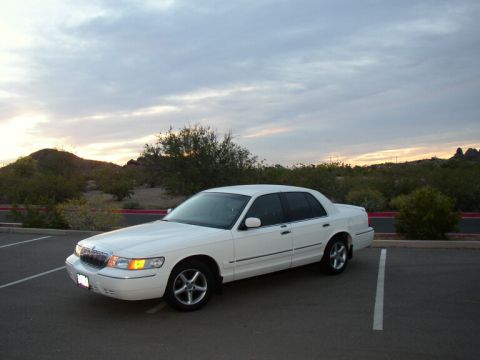 2001 Mercury Grand Marquis - A white 2001 Mercury Grand Marquis sedan is parked in a lot under a cloudy sky.