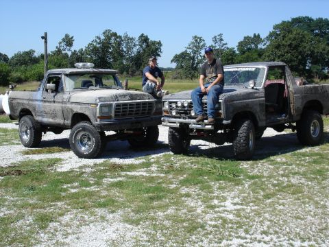 1979 Ford Bronco - Two lifted Ford trucks, likely from the late 70s or early 80s, are parked side-by-side in a grassy area.