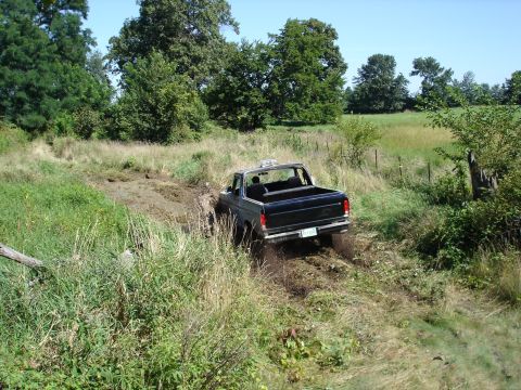 1979 Ford Bronco - A black 1978 Ford Bronco navigates a challenging muddy terrain on a sunny day.