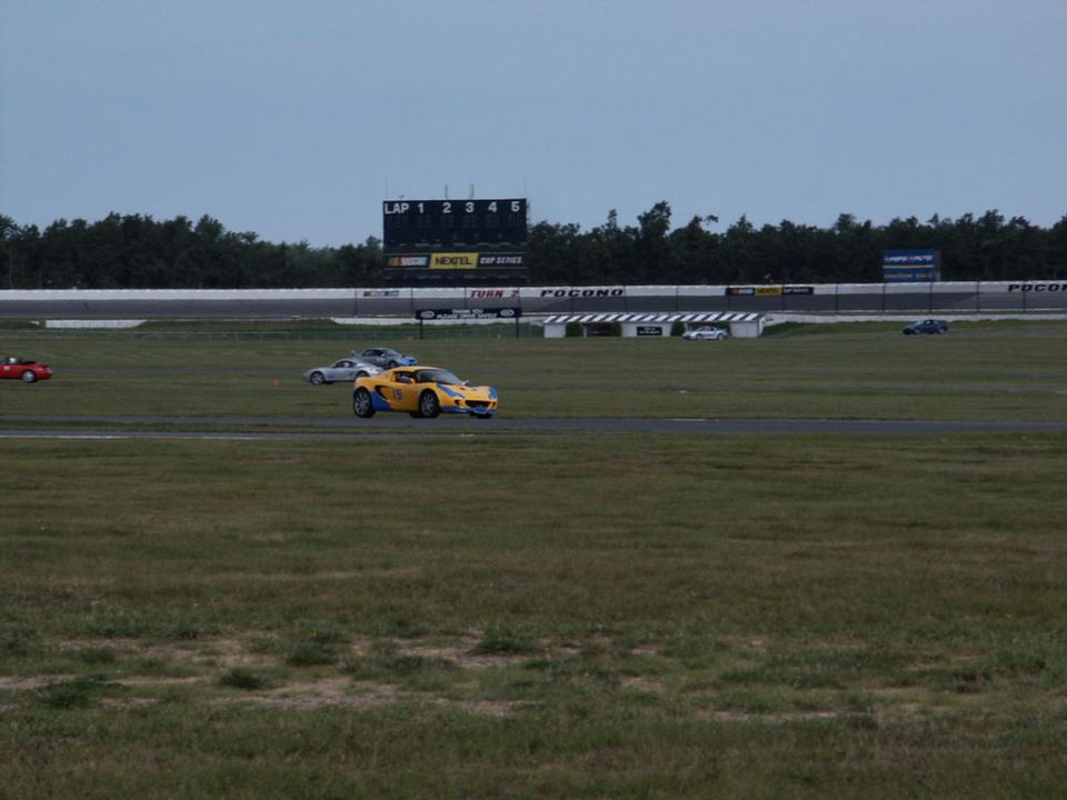 Yellow Lotus Elise on a race track with other cars and a scoreboard