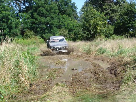 1979 Ford Bronco - A gray pickup truck navigates a muddy track, kicking up water and dirt.
