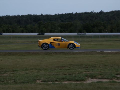 2001 Mercury Grand Marquis - A yellow Lotus Elise with blue accents races on a track, with other cars in the background.