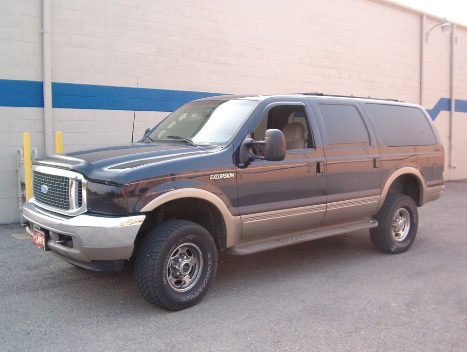 Dark blue and tan Ford Excursion SUV, front three-quarter view by a block wall