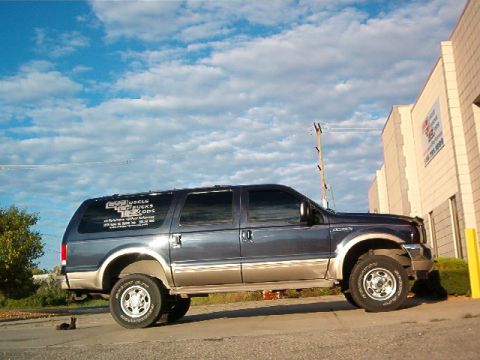 2000 Ford Excursion - A Ford Excursion is parked outside a building on a cloudy day. The vehicle has custom lettering on the rear door.