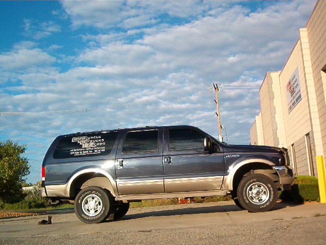 Lifted dark blue-gray Ford Excursion SUV, side view with shop window decals