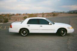2001 Mercury Grand Marquis - A white 2001 Mercury Grand Marquis is parked on a paved surface with a dry, hilly landscape in the background.