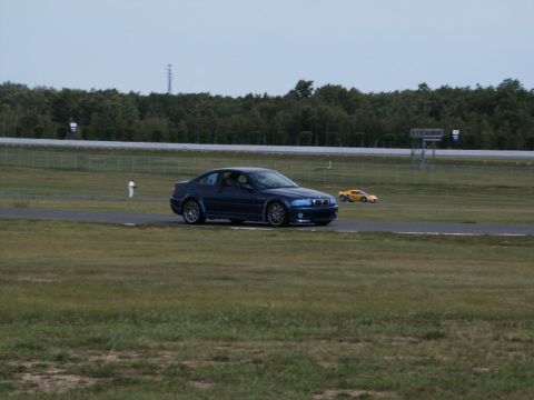 2001 Mercury Grand Marquis - A blue BMW coupe drives on a paved track with a yellow sports car in the distance.