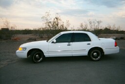 2001 Mercury Grand Marquis - A white 2001 Mercury Grand Marquis sedan is parked outdoors with a desert landscape behind it under a cloudy sky.
