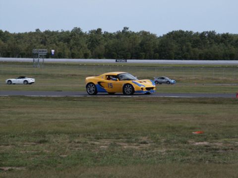 2001 Mercury Grand Marquis - A yellow Lotus Elise with blue racing stripes and the number 15 is seen on a race track with other vehicles in the background.