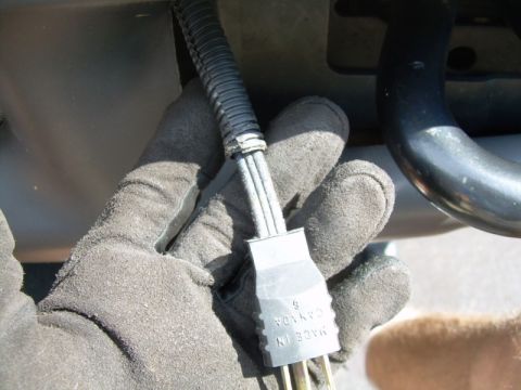 2002 Ford F-250 - Hand holding a black electrical connector with wires inside protective tubing.