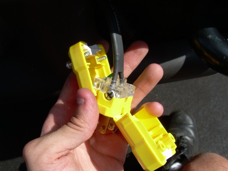 Hand holding an opened yellow electrical plug showing internal wiring, terminal block, and prongs