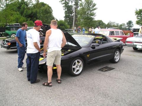 1984 Pontiac Fiero - A black 1994 Pontiac Firebird Trans Am is displayed with its hood up, surrounded by onlookers at a car show.