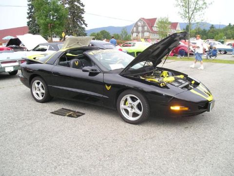1984 Pontiac Fiero - Black 1994 Pontiac Firebird with yellow accents at a car show.